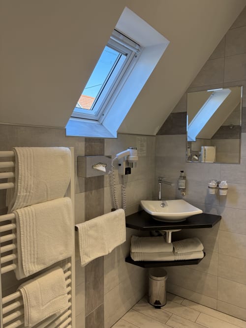 Salle de bain mansardée moderne à l'Hôtel de l'Ange avec lucarne, lavabo sur colonne, sèche-serviettes chauffant et vue sur le jardin