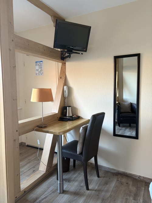Bureau d'hôtel avec téléviseur, lampe et chaise noire à l'Hôtel de l'Ange à Niedermorschwihr