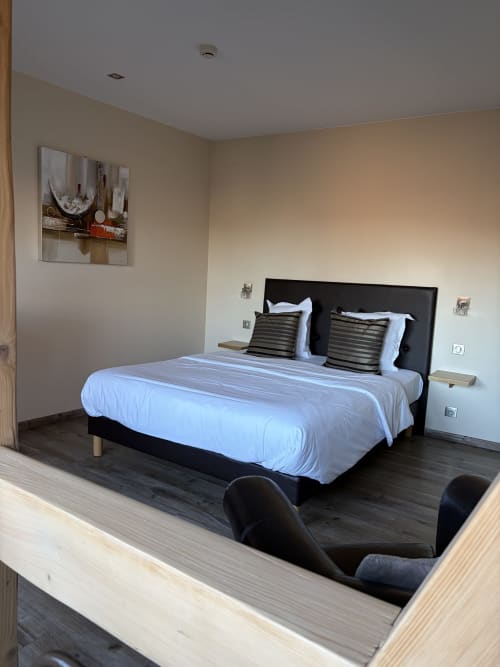 Chambre Tradition Double à l'Hôtel de l'Ange avec lit à structure noire, draps blancs et mobilier contemporain