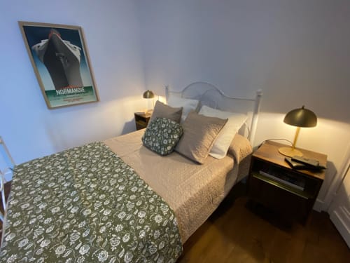 Chambre Art Déco au Prieuré de Saint-Pierre avec lit en métal blanc, linge à motifs, lampes en laiton et affiche vintage de bateau