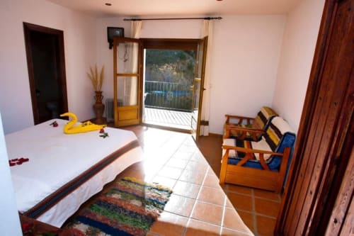 Bright bedroom at Hotel Mulhacén Trevélez with bed, wooden furniture, and balcony overlooking Granada mountains