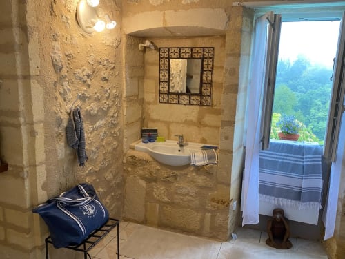 Rustic stone bathroom with sink, mirror, and terrace door overlooking lush gardens at Le Prieuré de Saint-Pierre