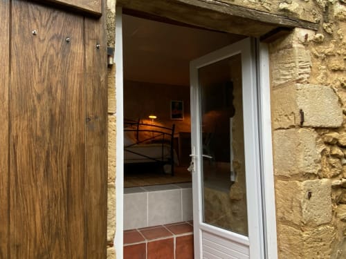 Entrance to Chambre 50's at Le Prieuré with white-framed glass door, terracotta tiles, and stone walls, garden view