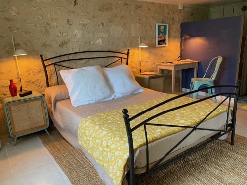 Chambre rétro années 1950 au Prieuré avec lit en métal, oreillers blancs, couverture à motifs jaunes et ambiance chaleureuse