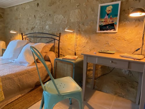 1950s-style bedroom at Le Prieuré with iron bed, desk, turquoise chair, and warm amber stone walls