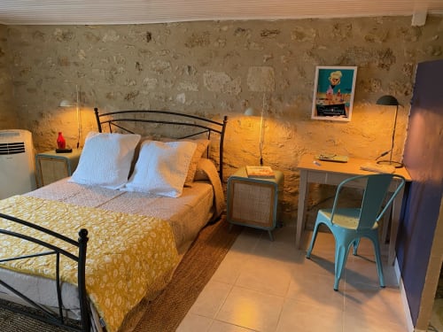 1950s-themed bedroom with stone walls, yellow bedding, blue chair, and garden view at Le Prieuré de Saint-Pierre boutique