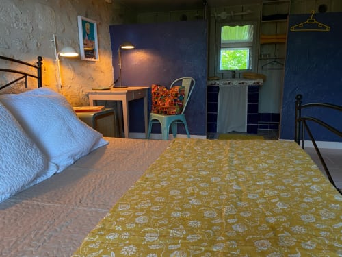 Charming 1950s-style bedroom at Le Prieuré with blue walls, golden patterned bedspread, desk, and garden view window