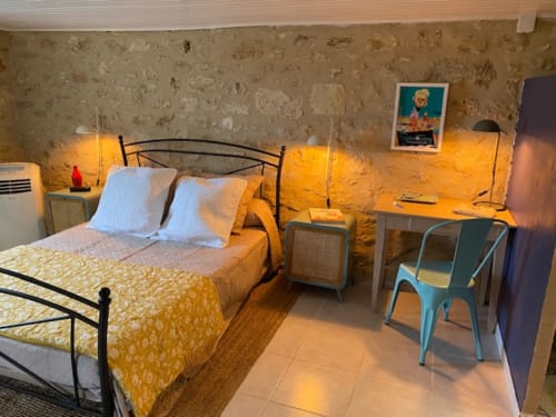 1950s-style bedroom at Le Prieuré de Saint-Pierre B&B with yellow bedspread, stone walls, warm lighting, and garden view