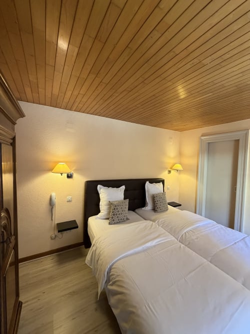 Chambre twin à l'Hôtel de l'Ange à Niedermorschwihr avec plafond en bois, literie blanche et éclairage ambiant.