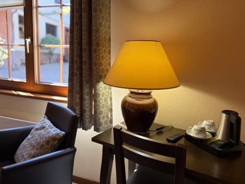 Chambre d'hôtel à l'Hôtel de l'Ange avec lampe jaune, mobilier sombre et vue sur Niedermorschwihr