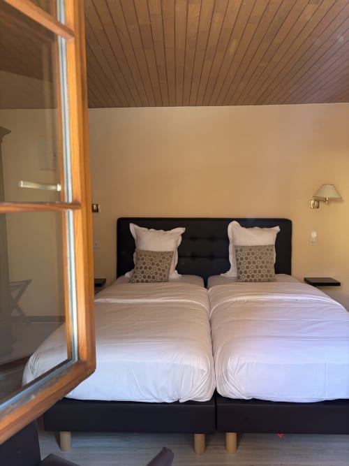 Chambre twin de l'Hôtel de l'Ange à Niedermorschwihr avec deux lits simples, tête de lit noire et plafond en bois