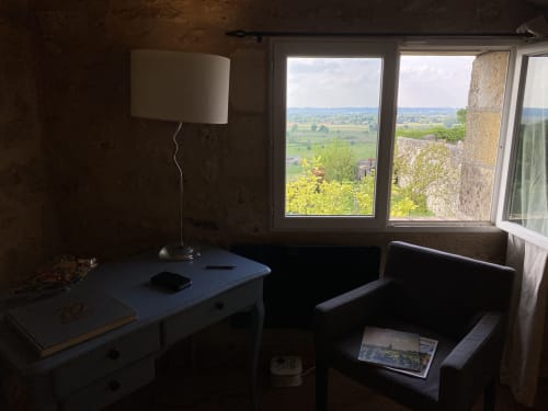 Bedroom at Le Prieuré de Saint-Pierre with desk, lamp, dark furniture, and garden view through windows overlooking French