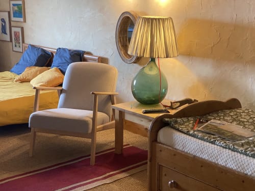 Cozy hotel room at Le Prieuré with beige armchair, green table lamp, wooden bed frame, and garden view in