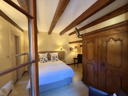 Chambre double classique de l'Hôtel de l'Ange avec poutres en bois, lit avec plaid bleu, armoire en bois et éclairage chaleureux