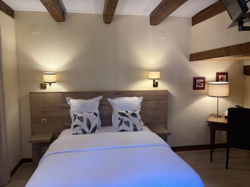 Chambre douillette de l'Hôtel de l'Ange avec lit double, poutres en bois, éclairage ambiant et bureau à Niedermorschwihr