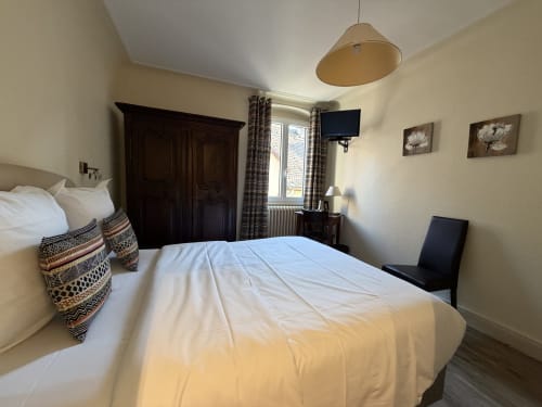 Chambre double lumineuse à l'Hôtel de l'Ange à Niedermorschwihr avec draps blancs, armoire en bois foncé et télévision écran plat