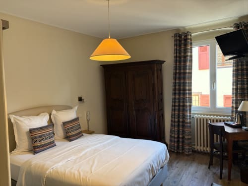 Chambre double à l'Hôtel de l'Ange à Niedermorschwihr : lit blanc, armoire foncée, lampe suspendue orange, espace de travail.