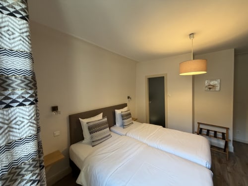 Chambre twin de l'Hôtel de l'Ange à Niedermorschwihr avec deux lits, rideaux géométriques et luminaires suspendus