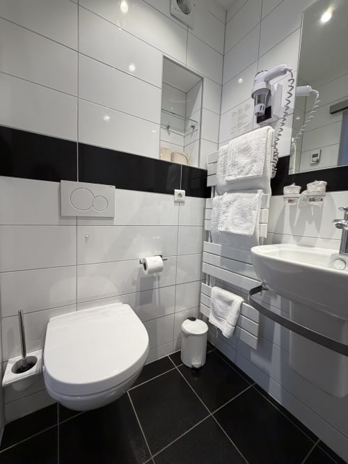 Salle de bain moderne de l'Hôtel de l'Ange à Niedermorschwihr avec carrelage blanc, accents noirs, toilettes, lavabo et radiateur sèche-serviettes