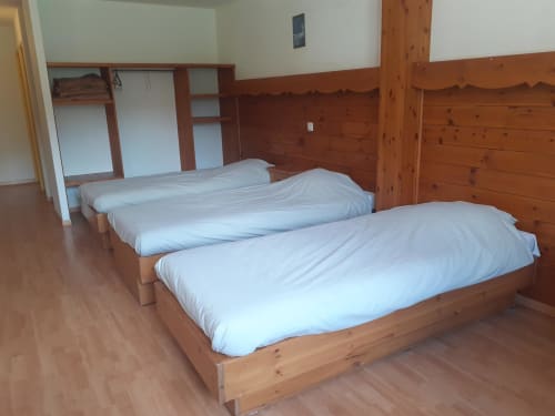 Chambre triple au Centre Sportif d'Altitude de Briançon avec lits en bois et literie blanche