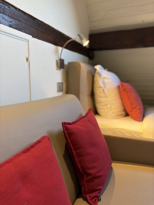 Chambre familiale cosy de l'Hôtel de l'Ange avec coussins rouges, literie jaune et poutres en bois sombre