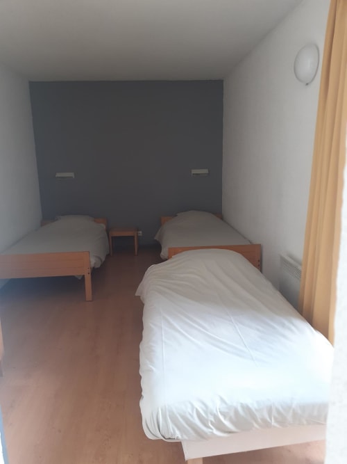 Chambre triple au Centre Sportif d'Altitude de Briançon avec lits simples en bois et tête de lit foncée