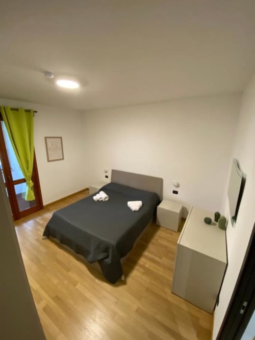 Camera moderna agli MiSaNi Apartments con letto scuro, pavimento in legno, scrivania e balcone con tende gialle