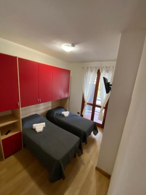 Camera matrimoniale presso MiSaNi Apartments con armadio rosso, letti scuri, pavimento in legno e porte-finestre in vetro