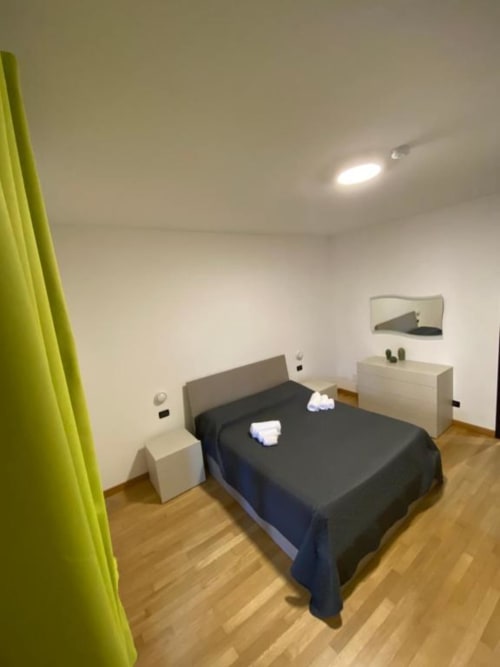 Camera moderna agli MiSaNi Apartments con letto nero, comodini bianchi, tende verde lime, pavimento in legno e design contemporaneo