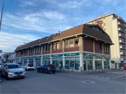 Facciata degli Appartamenti MiSaNi con edificio in laterizio, negozi al piano terra, auto parcheggiate e torre residenziale in Italia