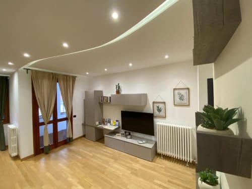 Soggiorno moderno con mobile TV, parquet, soffitto curvo con illuminazione incassata, piante in vaso e porte-finestre