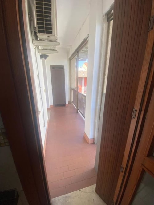 Stretto corridoio negli Appartamenti MiSaNi con pavimento in cotto, porte in legno e vista sul balcone in fondo