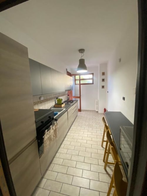 Cucina moderna in stile lineare negli Appartamenti MiSaNi con mobili bianchi, piano di lavoro nero, zona pranzo e illuminazione a sospensione
