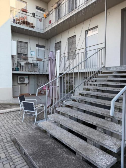 Cortile MiSaNi Apartments con scalinata in pietra, ringhiere metalliche, area giardino con sedute e edificio residenziale su più livelli.