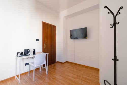 Camera moderna dell'Hotel Centrale Bologna con scrivania, sedia, TV a parete, porta in legno e appendiabiti su pavimento in legno
