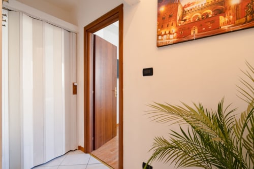 Ingresso moderno della camera d'hotel al Centrale Bologna con porta in legno, armadio bianco e pianta verde