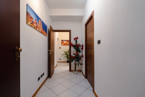 Corridoio della Centrale Bologna B&B a Bologna, Italia, con porte in legno, pareti bianche e fiori rossi in un vaso