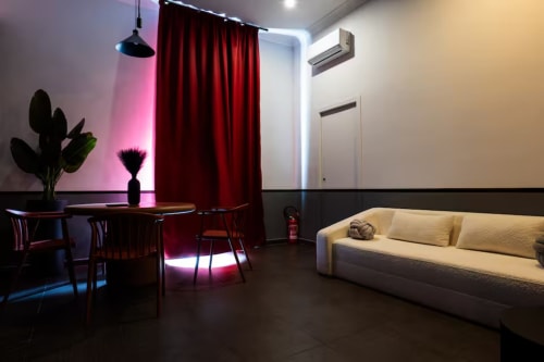 Suite moderna urbana presso LH51 Rooms a Napoli con zona pranzo illuminata di rosa, tende rosse e divano color crema