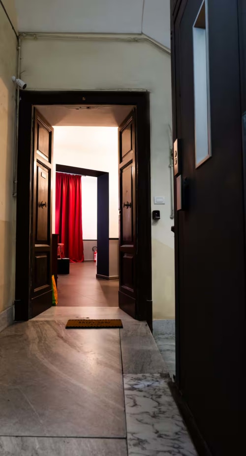 Doppie porte in legno scuro che si aprono su una sala con tende rosse nella suite LH51 di Napoli