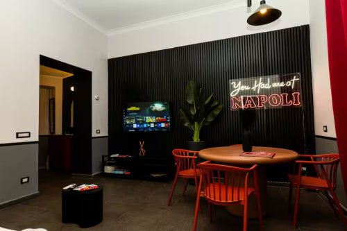 Suite moderna presso LH51 Napoli con sedie rosse, tavolo in legno, smart TV e insegna neon 'You Had me at Napoli'