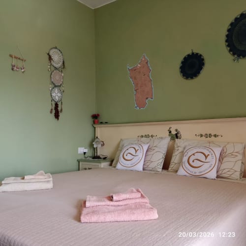 Sardinian-themed bedroom with green walls, decorated with dream catchers and cork map, featuring dressed bed with decorative