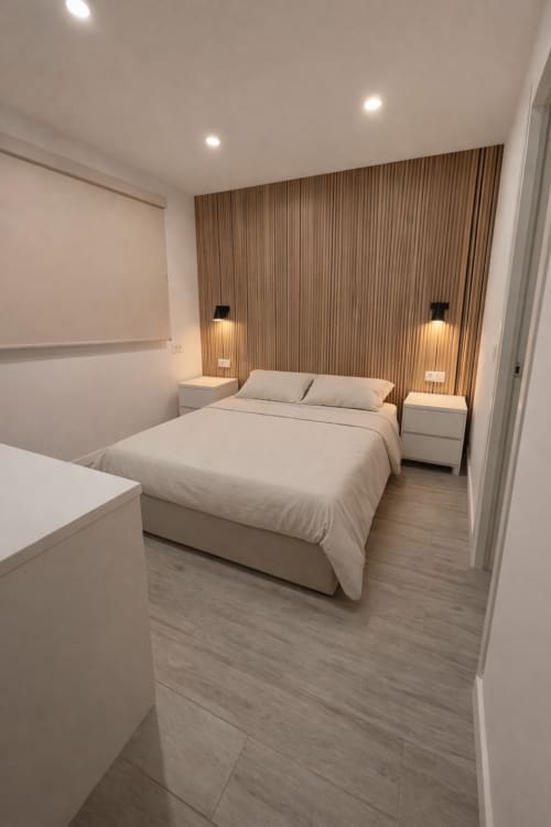 Moderno dormitorio doble en El Chalecito de Alicante con ropa de cama beige, pared de madera y luminarias contemporáneas