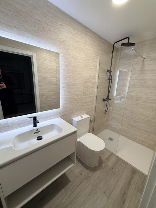 Baño moderno en el hotel El Chalecito de Alicante con lavabo, inodoro y ducha con mampara de cristal
