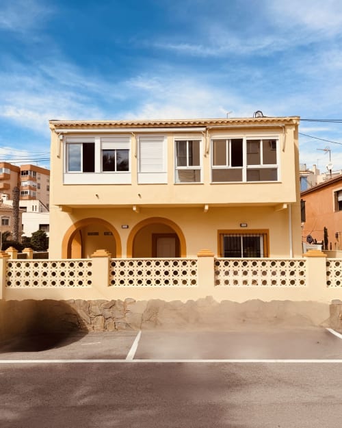 Fachada del hotel frente al mar El Chalecito de Alicante con muros amarillos, terrazas arqueadas y ventanas modernas