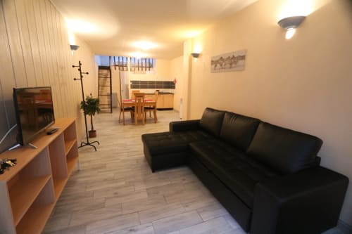 Studio avec salon aménagé d'un canapé noir, TV, table à manger en bois et kitchenette à l'Appart'Hôtel Résidence de Cholet