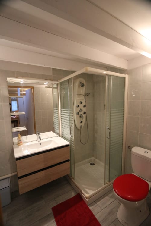 Salle de bain moderne de l'Appart'Hôtel Résidence de Tourisme de Cholet avec douche spacieuse, meuble vasque en bois, toilettes et touches rouges