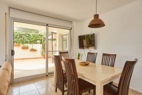 Comedor moderno con sillas de madera, mesa color crema y acceso a terraza en Experiencias Encant, Calafat
