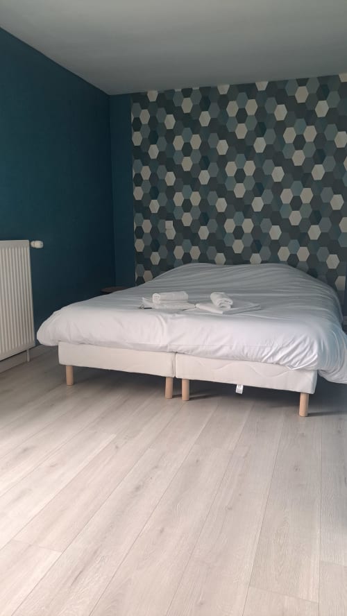 Chambre moderne aux murs bleu-vert, accent hexagonal, parquet clair et lit crème à l'Appart'Hôtel