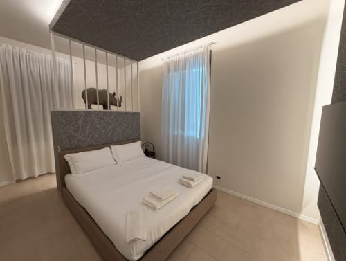 Modern bedroom at DV Garda Suite in Campione with queen bed, white linens, dark patterned headboard, sheer curtains, and