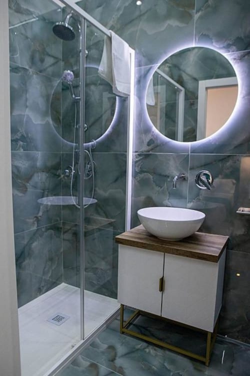 Bagno moderno del B&B Dreams & Colors Napoli con piastrelle in marmo verde, specchi rotondi illuminati a LED, lavabo bianco e vetro